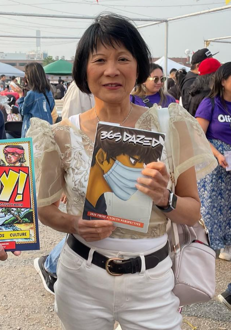 Smiling woman at an outdoor festival holding a comic magazine with a masked character on the cover.