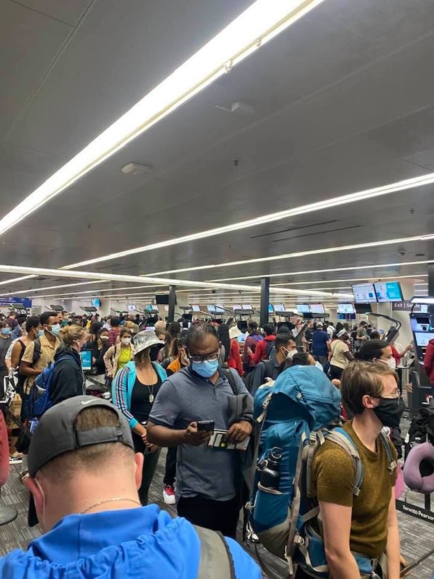 Picture11 - The Canada Times Crowded airport check-in area with travelers wearing masks and backpacks under bright lights.