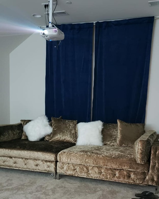 Picture23 - The Canada Times Living room theater setup: ceiling-mounted projector above a brown velvet sectional sofa with white fluffy pillows and dark blue curtains in the background.