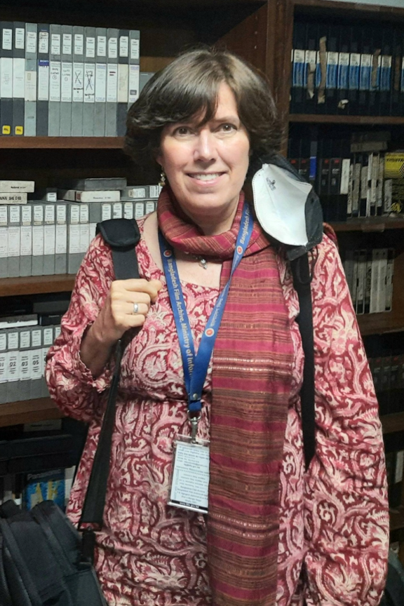 Picture35 - The Canada Times Smiling woman in a pink patterned sweater in a library, wearing a blue lanyard with a badge and a backpack.