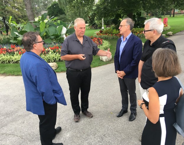 Picture8 - The Canada Times Five adults stand on a park path in a garden, having a conversation as one man gestures with his hands.