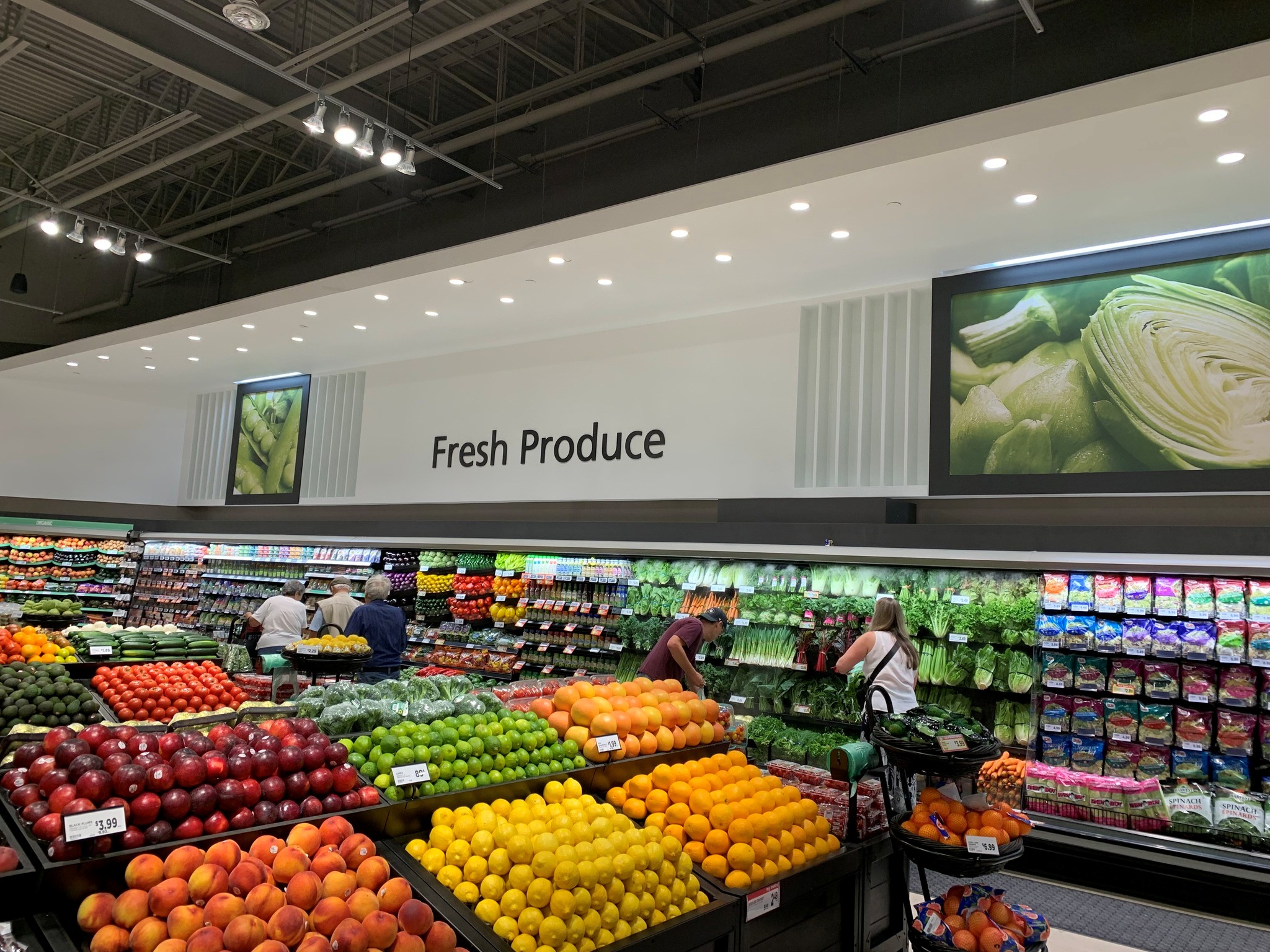 1 - The Canada Times Wide view of a grocery store produce section with colorful fruits and vegetables on display and a large 'Fresh Produce' sign overhead, shoppers browsing.