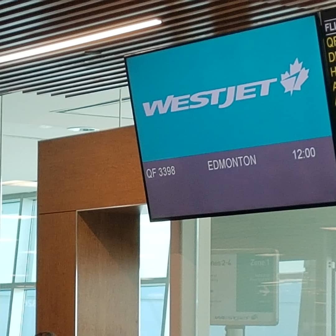 11 - The Canada Times Airport gate display with WestJet logo showing flight QF 3398 to Edmonton at 12:00.