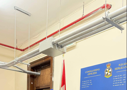 2 - The Canada Times Industrial interior with exposed silver and red pipes above a doorway and a blue plaque listing commanding officers nearby.