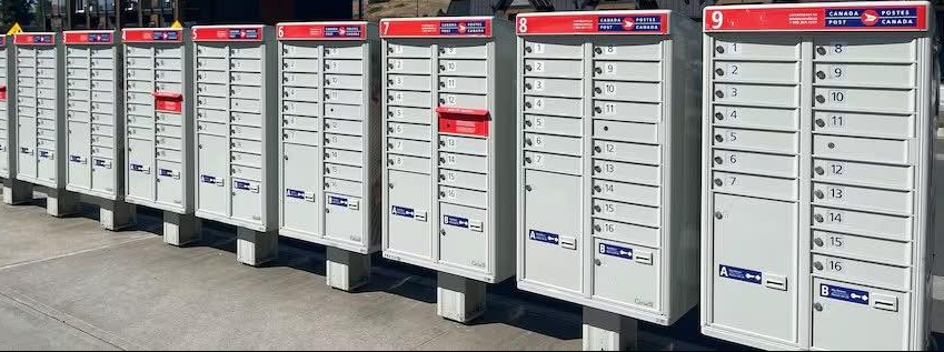 9 - The Canada Times Row of gray public mailboxes with numbered doors and red top labels at a sidewalk site.