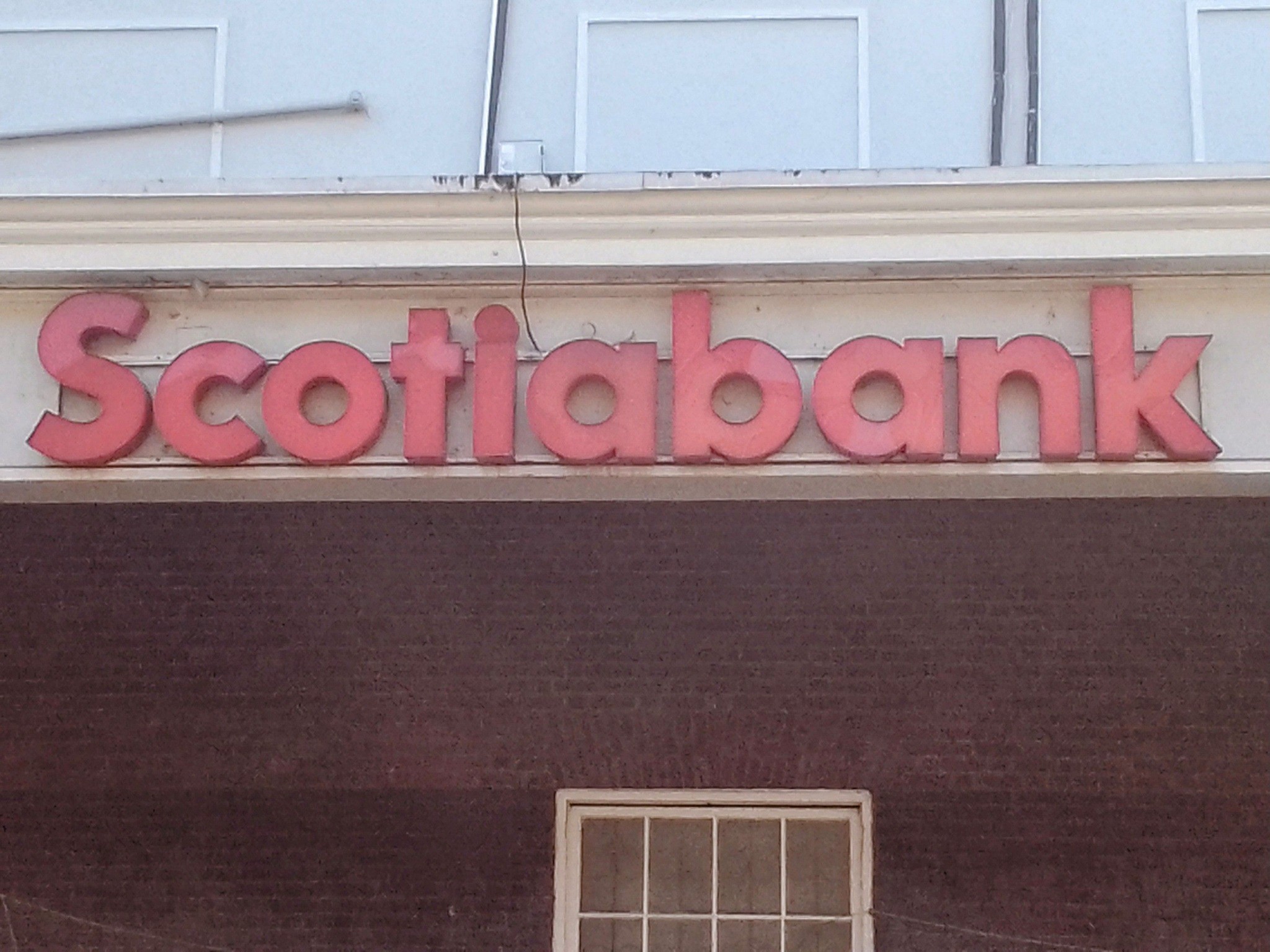 1 - The Canada Times Partial view of a storefront sign reading 'Scotiabank' in large pink letters above a window on a dark purple wall.