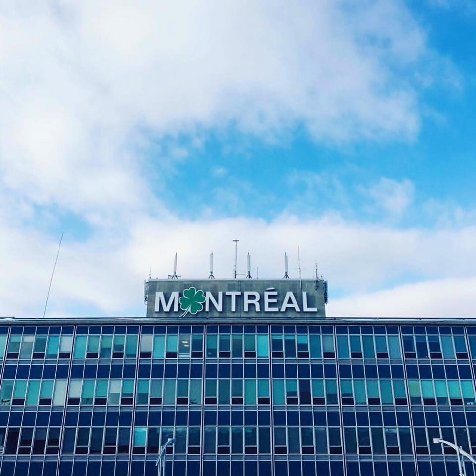1 - The Canada Times Glass-fronted office building with a large MONTRÉAL sign on the roof against a blue sky.