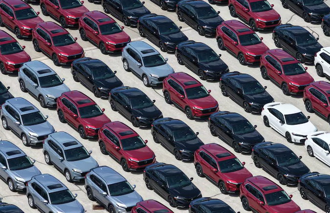 10 - The Canada Times Aerial view of a parking lot filled with diagonally arranged rows of red, blue, gray, and white compact cars.
