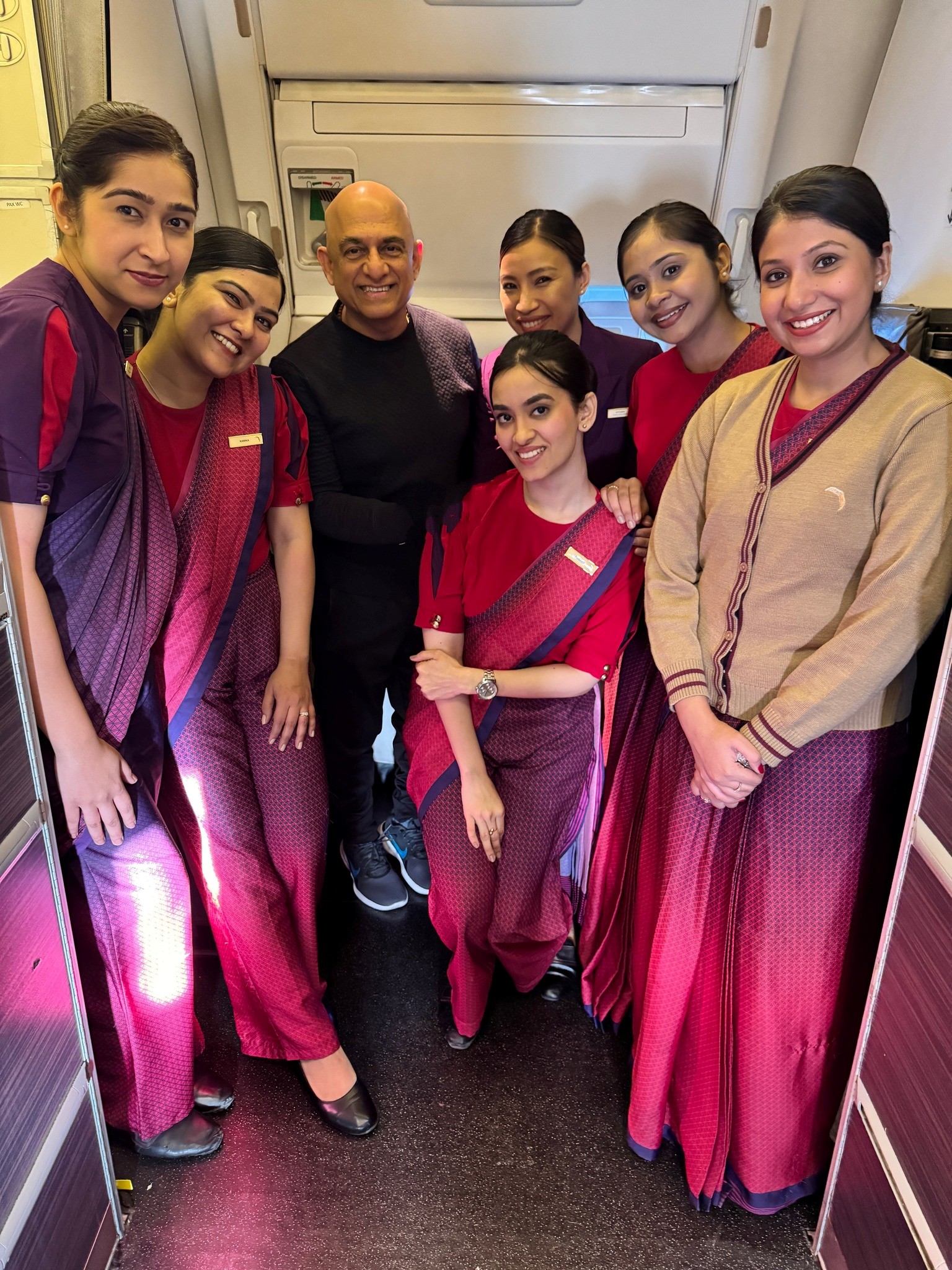 12 - The Canada Times Group of airline crew and a passenger posing together in an airplane cabin, all smiling in the aisle.