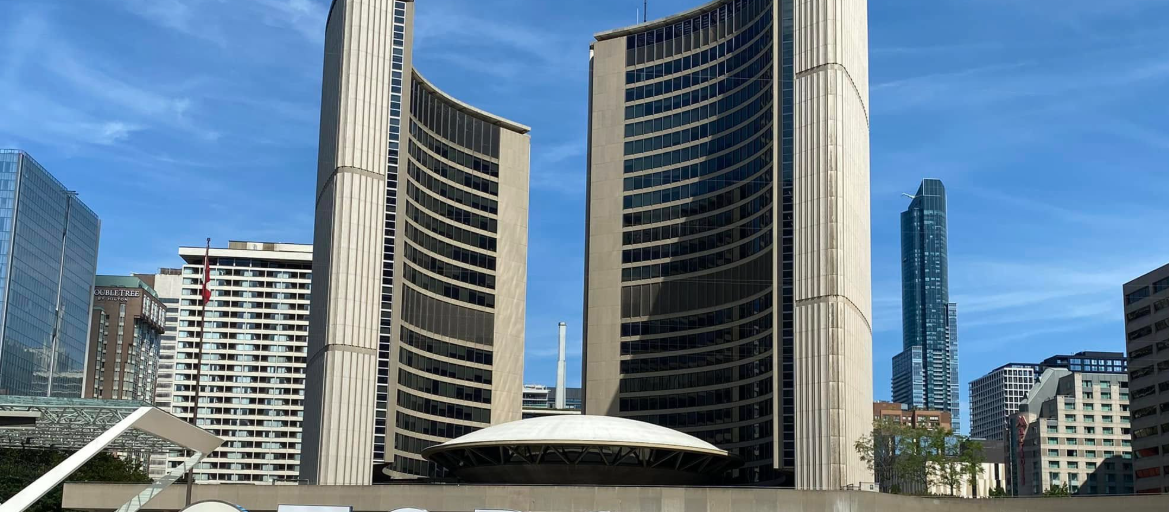 13 - The Canada Times Two tall curved office towers with a white-domed, low building in front against a bright blue sky.