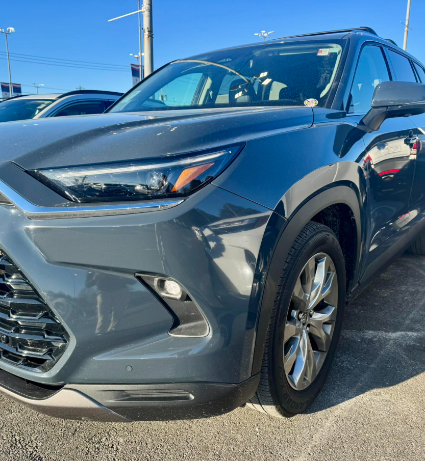 2 - The Canada Times Front-right corner of a metallic blue SUV, showing the headlight, grille, and front wheel in a car dealership lot.