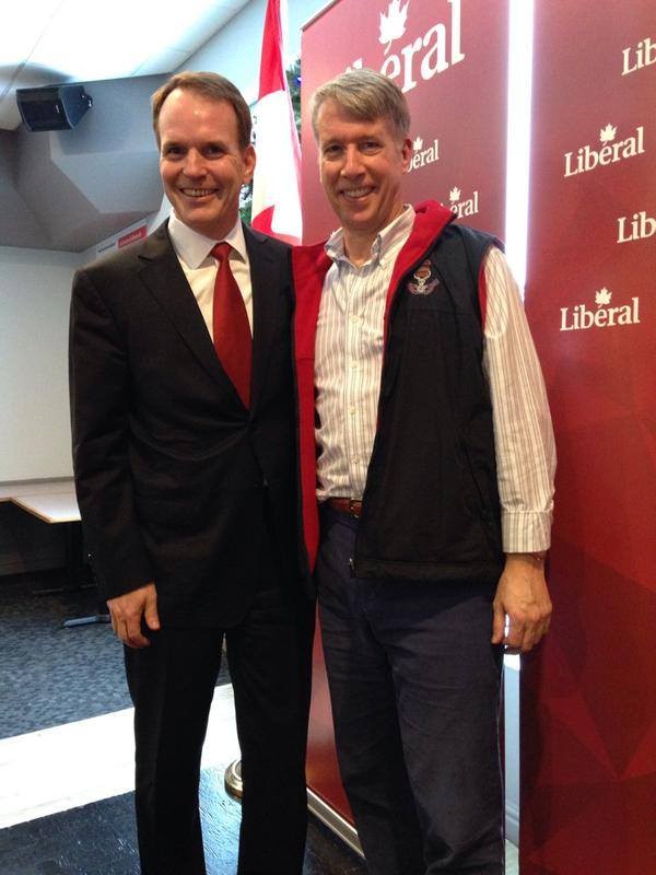 Two men smiling for a photo at a Liberal party event, standing in front of a red Liberal backdrop.