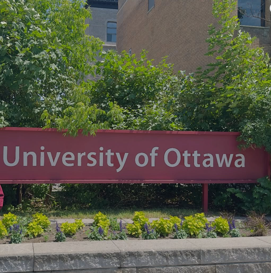 Maroon sign reading 'University of Ottawa' with green shrubs and a flower bed in front.