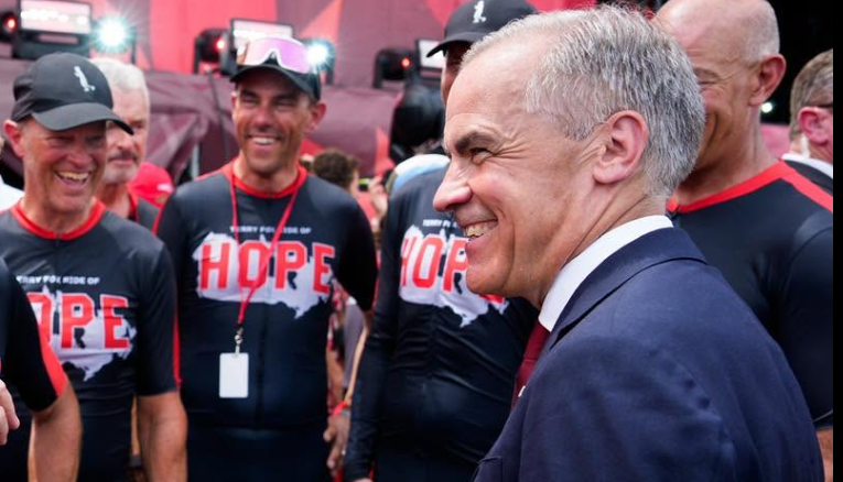 11 - The Canada Times Smiling man in a dark suit and red tie chats with volunteers wearing black HOPE shirts at a charity event.