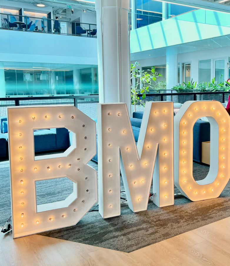13 - The Canada Times Large illuminated letters spelling 'BMO' in a modern office lobby area with blue seating in the background.