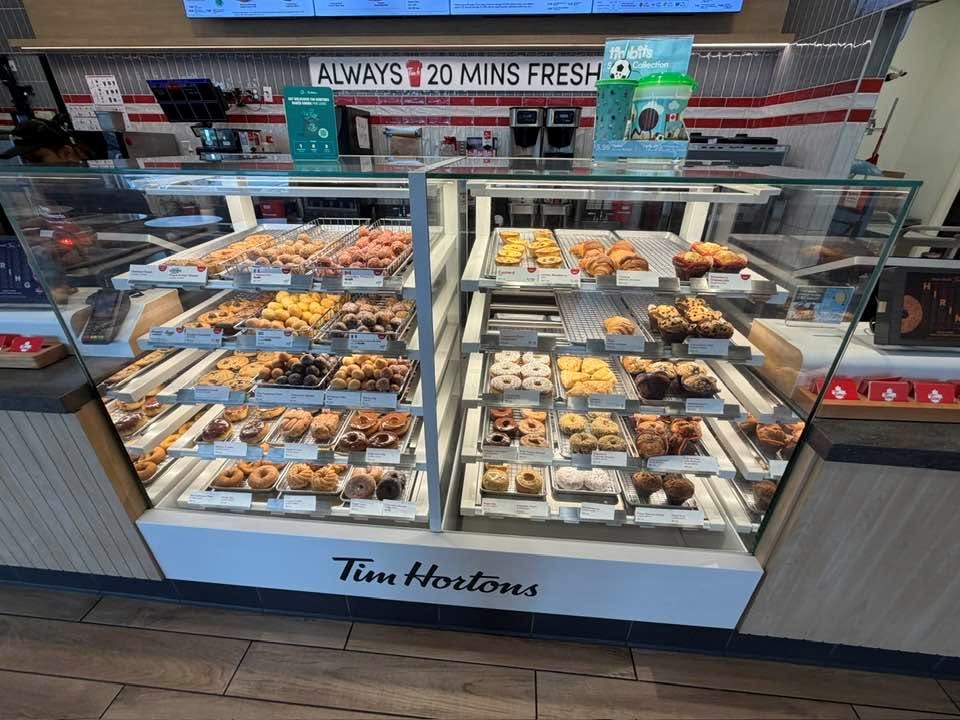 Glass-front Tim Hortons pastry display case filled with assorted donuts and pastries in trays built for self-serve selection.