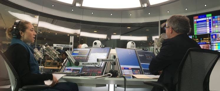 2 - The Canada Times Two broadcasters wearing headphones sit at a Bloomberg Radio studio desk with microphones and multiple screens in front of them.