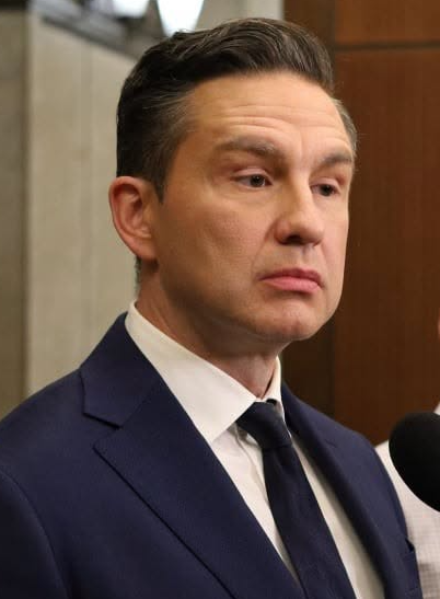 Man in a navy suit and dark tie at a microphone, looking serious during a press conference.