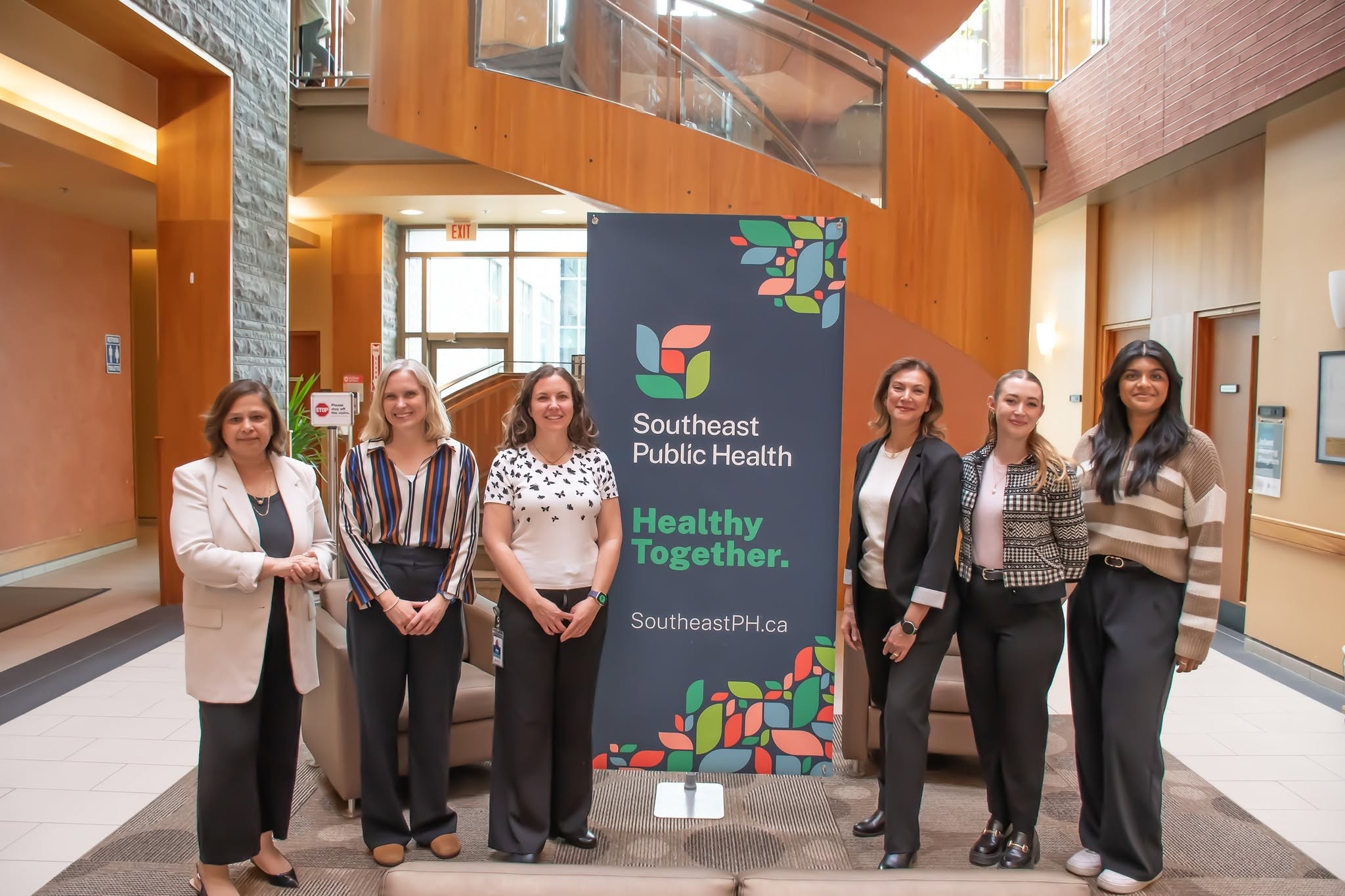 4 - The Canada Times Group of six professionals posing in a lobby beside a Southeast Public Health banner reading "Healthy Together" and the website SoutheastPH.ca