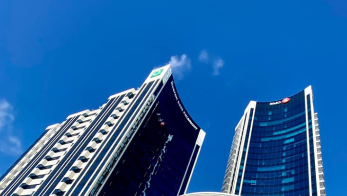 5 - The Canada Times Two modern skyscrapers with glass facades reach toward a clear blue sky, reflecting sunlight in an urban skyline.