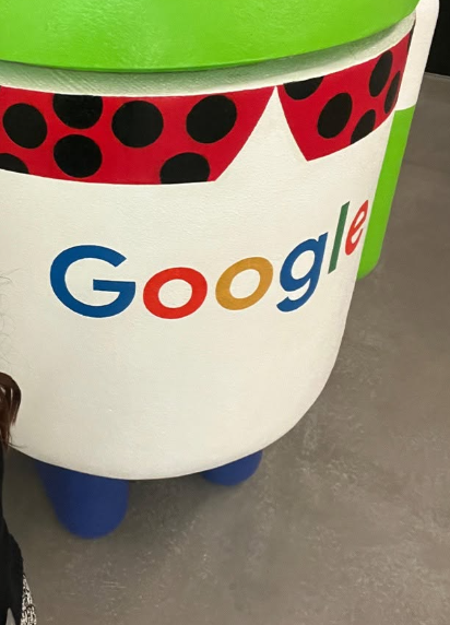 7 - The Canada Times Close-up of a white Android-style statue with Google's multicolor logo on its torso, a red polka-dot sash, and blue feet against a gray floor.