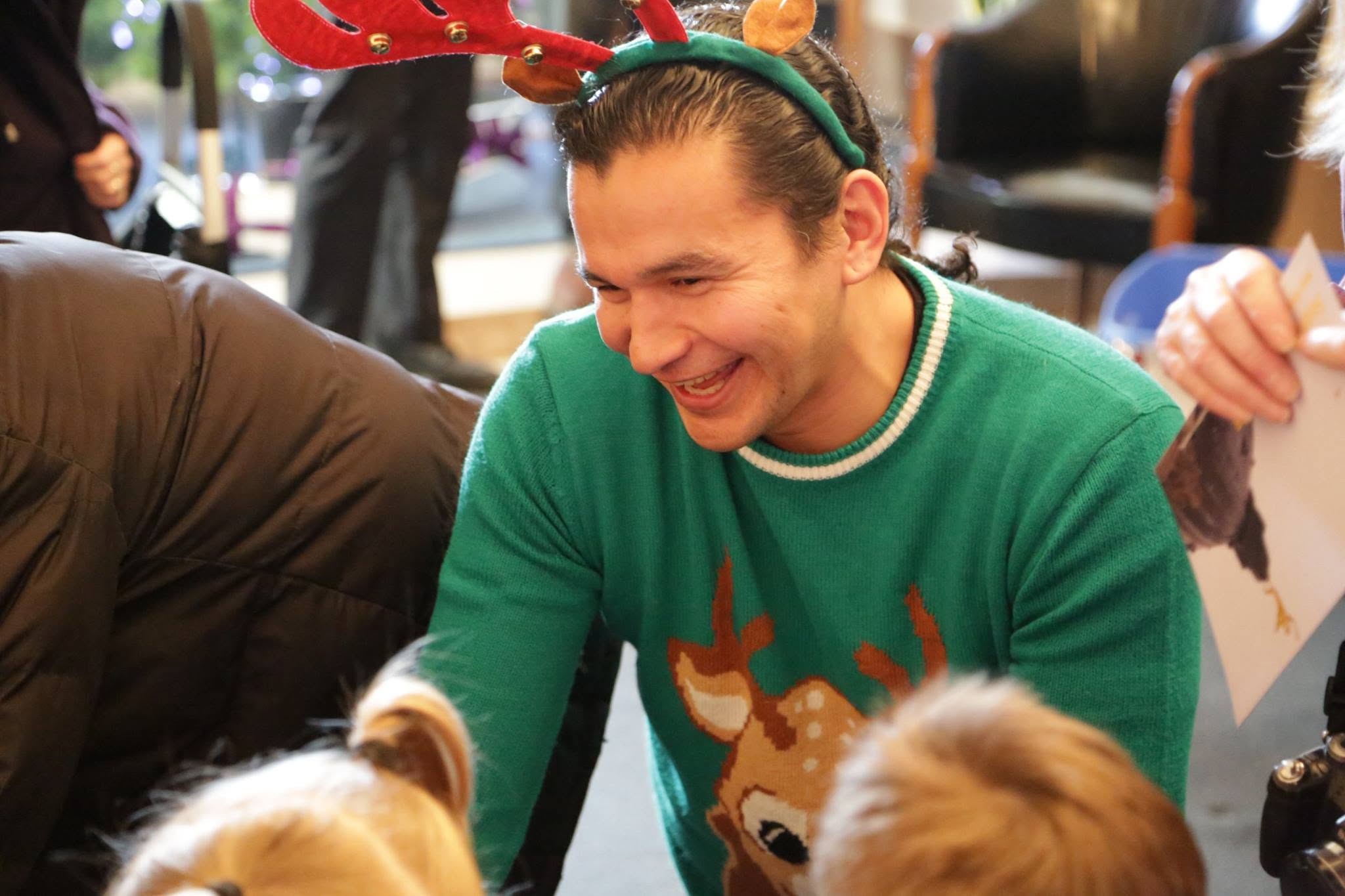 9 - The Canada Times Man wearing a reindeer-antler headband and green Christmas sweater, smiling at a festive gathering.