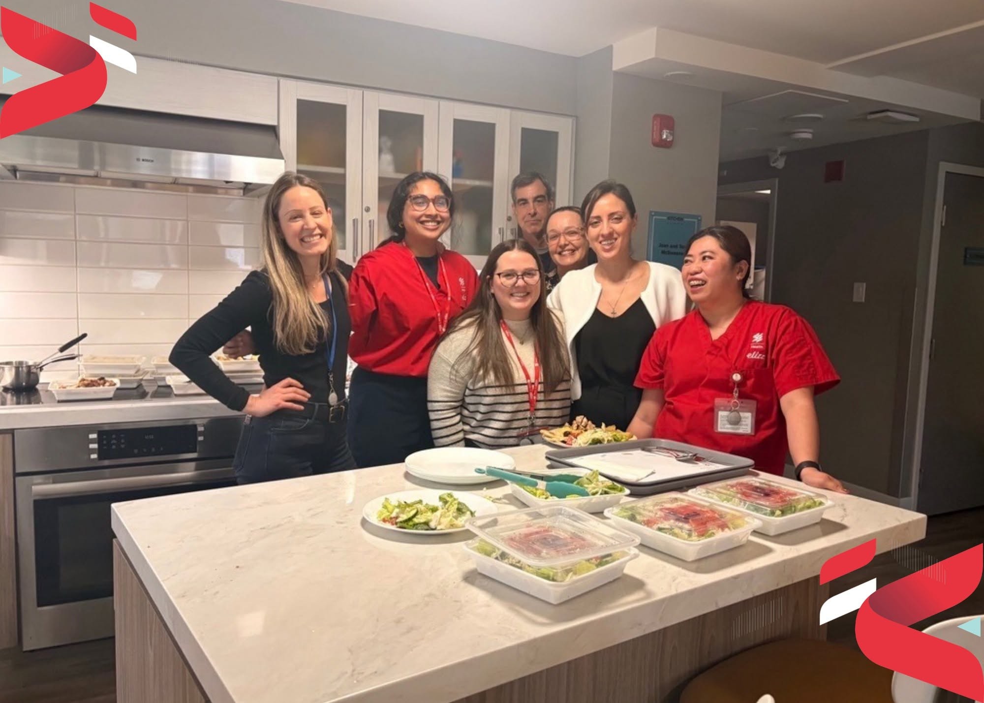 1 - The Canada Times Group of colleagues in a kitchen smiling around a counter with prepared salads on plates and trays in front of them.