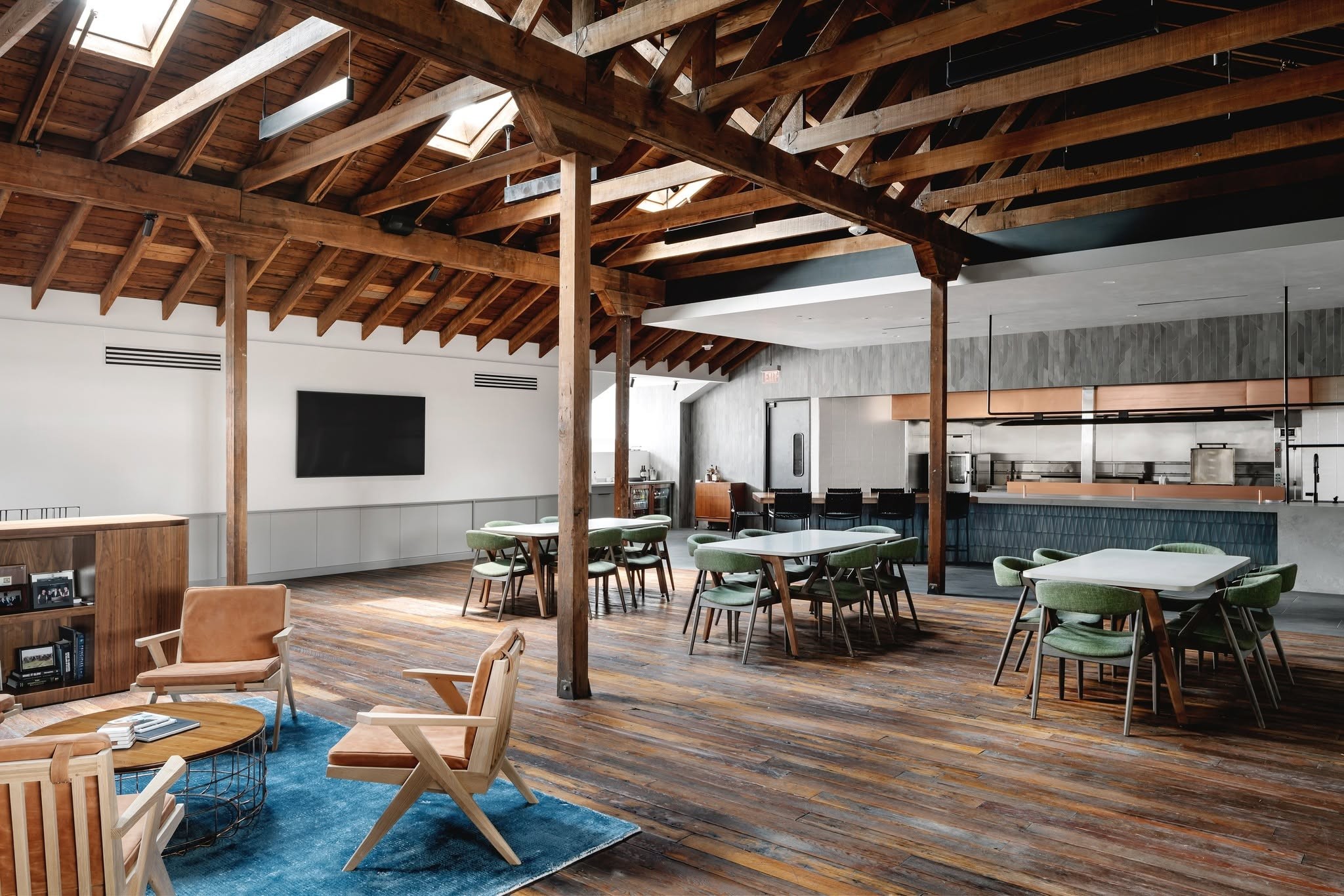 10 - The Canada Times Open-plan cafe or coworking space with exposed timber beams, skylights, and clustered tables and chairs. Kitchen area visible at the back.