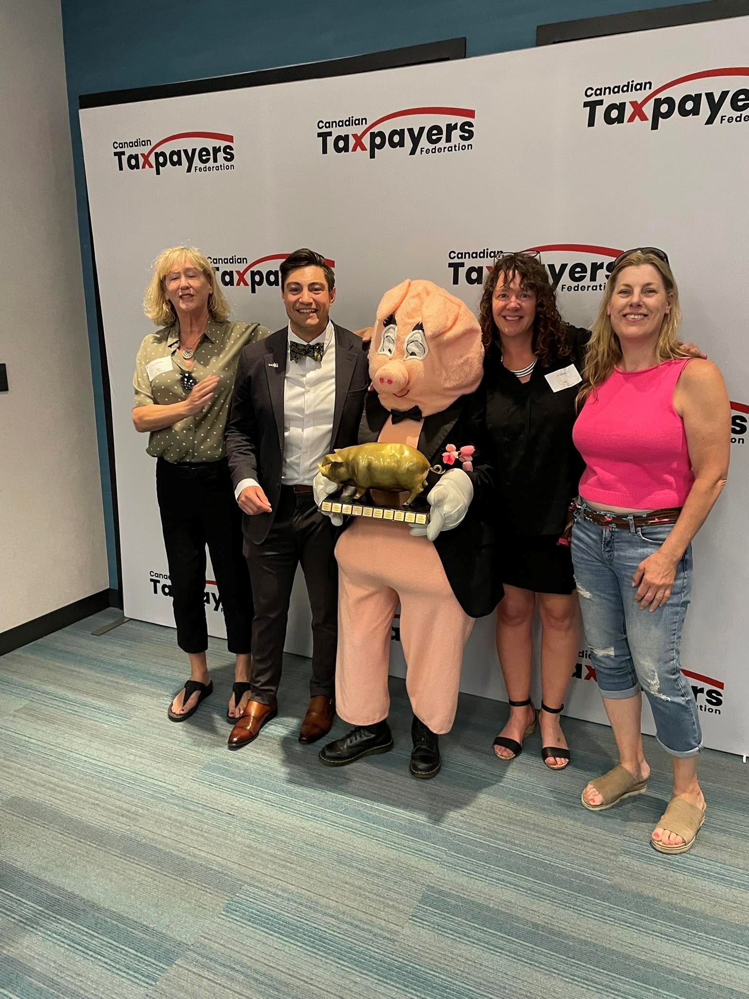 10 - The Canada Times Group of five adults posing for a photo with a pig mascot in a tuxedo at a Canadian Taxpayers Federation event backdrop.