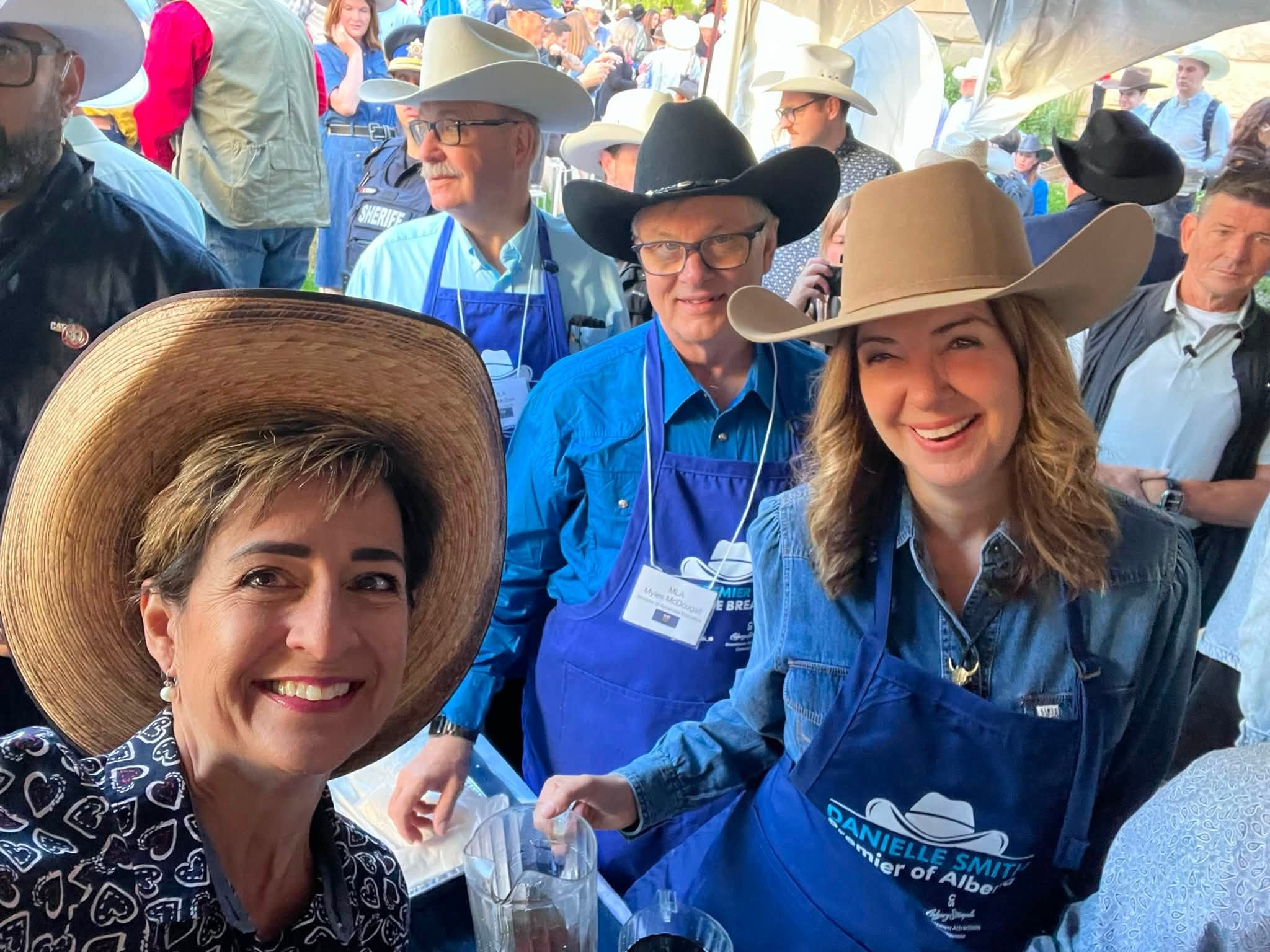 11 - The Canada Times Smiling woman in a wide-brim hat in the foreground, surrounded by people in cowboy hats at an outdoor western-themed event.