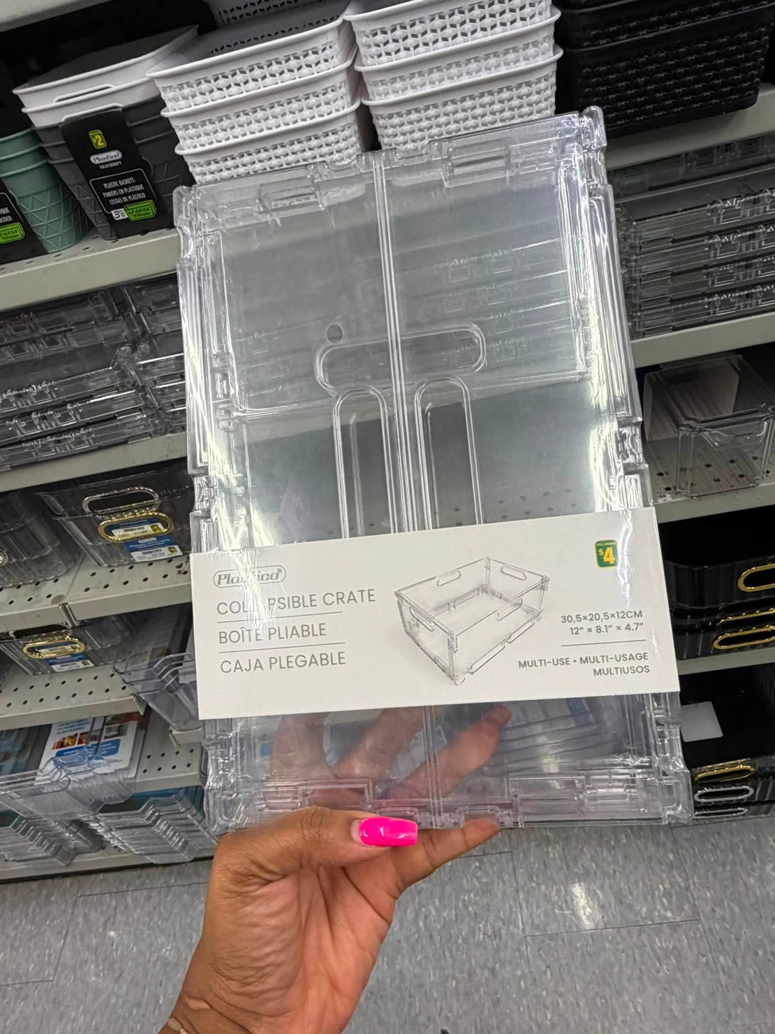 4 - The Canada Times Clear plastic collapsible crate held in a shopper's hand in a store, showing its interlocking sides and packaging text (30.5×20.5×12 cm).