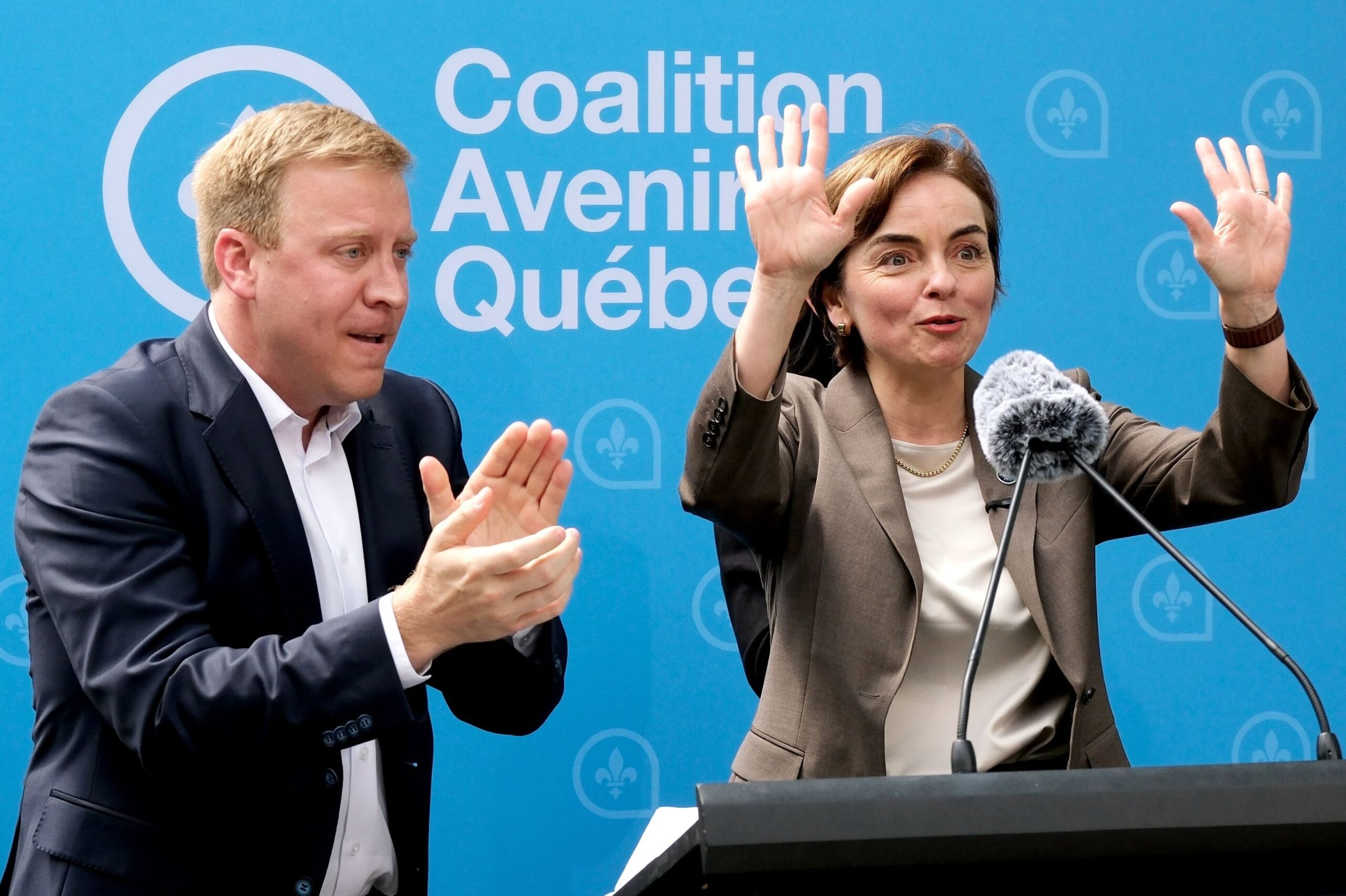 4 - The Canada Times Two adults at a press conference, one man and one woman, raising their hands in front of a blue Coalition Avenir Québec backdrop.