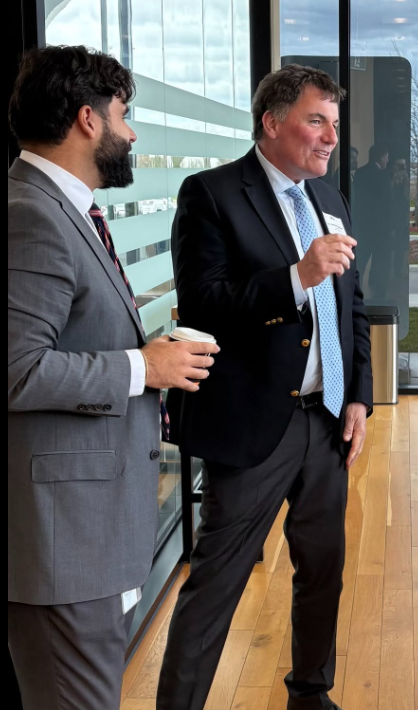 4 - The Canada Times Two businessmen in suits chat by a glass wall, one holding a coffee cup and gesturing as he speaks.