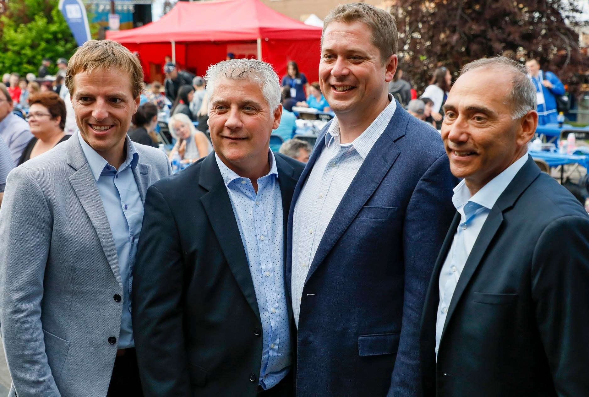 6 - The Canada Times Four men in suits smiling for a photo at an outdoor event with a red tent in the background.